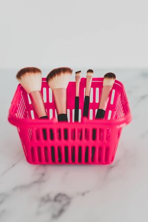 beauty industry and essential products concept, pink shopping basket with variety of make-up brushes in it for face and eye make-upの写真素材
