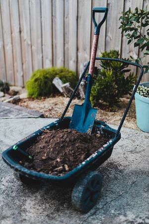 shovel and soil on wheelbarrow with backyard plants in the background shot at shallow depth of fieldの写真素材