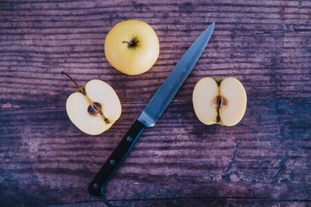 healthy plant-based food ingredients concept, apple halves on wooden table next to whole apples with knifeの写真素材