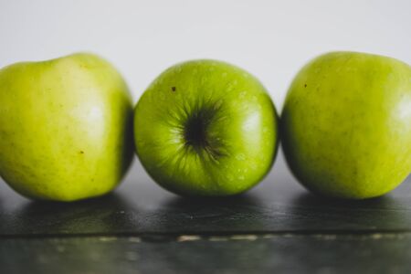 healthy plant-based food ingredients concept, green apples lined up on wooden table shot from eye-level perspectiveの写真素材