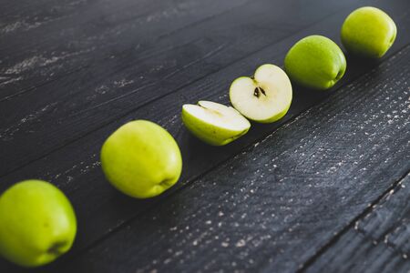 healthy plant-based food ingredients concept, green apples ined up on wooden table with some cut in halfの写真素材