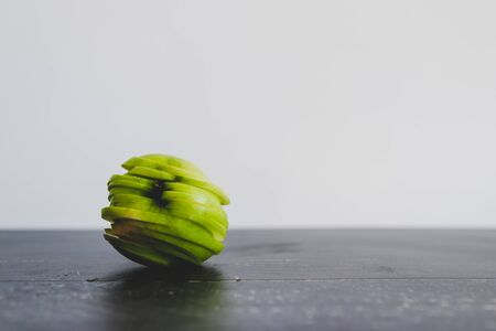 healthy plant-based food ingredients concept, green apple cut into thin equal slices stacked to maintain its original shapeの写真素材