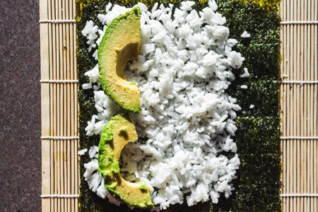 healthy plant-based food recipes concept, vegan avocado sushi getting prepared on roller 