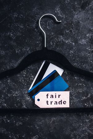ethical fashion concept, velvet clothes hanger with Fair Trade label and credit cards on it on black backgroundの写真素材