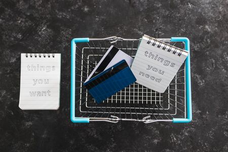 budgeting and shopping concept, things you need vs things you want notepads in shopping basket with...
