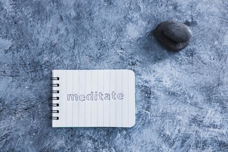self-care and mental health concept, notepad with text Meditate next to zen pebbles on grey concrete surfaceの写真素材