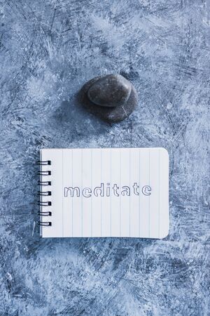 self-care and mental health concept, notepad with text Meditate next to zen pebbles on grey concrete...