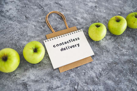 the new normal after covid-19, Contactless Delivery text on notepad among apples and with shopping bag concept of groceries shopping during quarantine or lockdownの写真素材