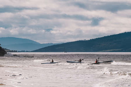HOBART, AUSTRALIA - July 5th, 2020: view of Kingston Beach on a cloudy winter day with people on kayaks in the water, the area is a popular suburb south of Hobart the capital city of Tasmaniaのeditorial素材