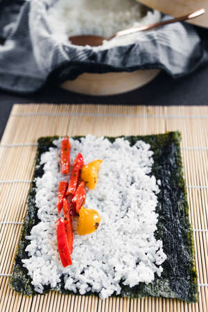 healthy plant-based food recipes concept, vegan sushi with seaweed and sticky rice with capsicum getting prepared on kitchen counterの写真素材