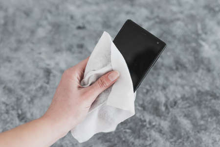 the new normal after covid-19 and concet of sanitizing surfaces, hand cleaning smartphone with disinfectant wipe to flatten the curve and prevent viruses and bacteriaの写真素材