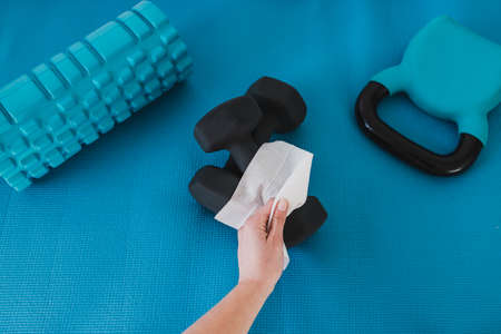 the new normal for businesses after covid-19, hand cleaning gym equipment with disinfectant wipe...