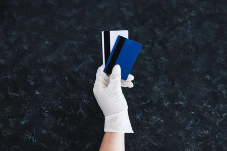 the new normal after the covid-19 virus pandemic outbreak, hand holding payment cards with disposable gloves on in order not to touch potentially infected surfacesの写真素材