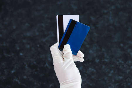 the new normal after the covid-19 virus pandemic outbreak, hand holding payment cards with disposable gloves on in order not to touch potentially infected surfacesの写真素材