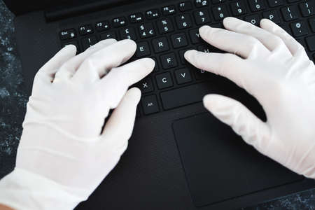 the new normal after thecovid-19 virus pandemic outbreak, hands typing on shared computer keyboard at work wearing disposable gloves to avoid contact with potentially infected surfacesの写真素材