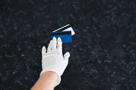 the new normal after the covid-19 virus pandemic outbreak, hand holding payment cards with disposable gloves on in order not to touch potentially infected surfacesの写真素材