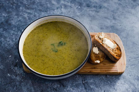healthy plant-based food recipes concept, zucchini pesto soup with bread and vegan butter on cutting...