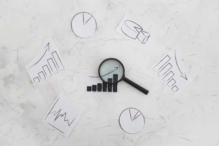 business analysis and statistics concept, desk with mixed graphs and charts with magnifying glass on itの写真素材