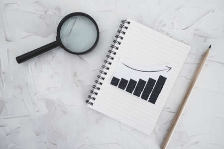 business analysis and statistics concept, desk with mixed graphs and charts on notebook with magnifying glass on itの写真素材