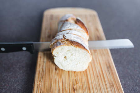 simple food ingredients concept, piece of baguette bread on cutting board with knife slicing it