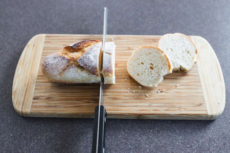simple food ingredients concept, piece of baguette bread on cutting board with knife slicing it