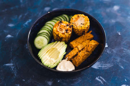 healthy plant-based food recipes concept, nourish bowl with avocado cucumber polenta chips and spicy...