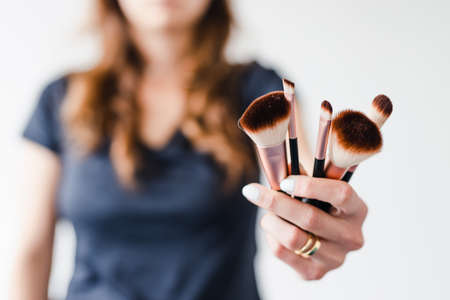 girl holding make-up brushes in front of the camera showing the product shot at shallow depth of field, concept of beauty bloggers and influencers recommanding products or making online make-up tutorials,の写真素材