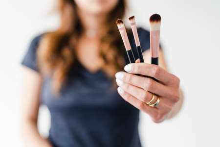 girl holding make-up brushes in front of the camera showing the product shot at shallow depth of field, concept of beauty bloggers and influencers recommanding products or making online make-up tutorials,の写真素材