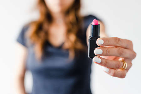 girl holding lipsticks in front of the camera showing the product shot at shallow depth of field, concept of beauty bloggers and influencers recommanding products or making online make-up tutorials,の写真素材