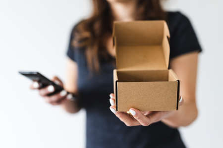 concept of home deliveries and online shopping, woman holding delivery parcel towards the camera while browsing on her smartphone shot at shallow depth of fieldの写真素材