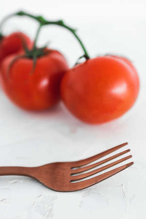 simple ingredients and whole food diet concept, close-up of three tomatoes on vine with fork next to...