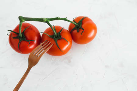 simple ingredients and whole food diet concept, close-up of three tomatoes on vine with fork next to them on white minimalist backgroundの写真素材