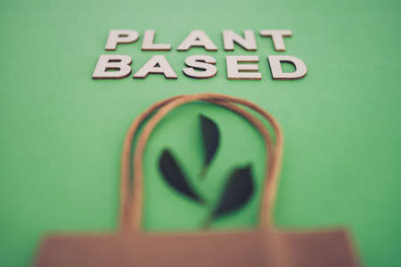 sustainable consumer choices for the environment, plant-based text with shopping bag and leaves on minimalist green backgroundの写真素材