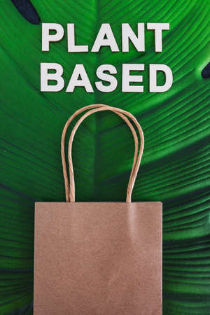 sustainable consumer choices for the environment, plant-based text with shopping bag on big tropical...