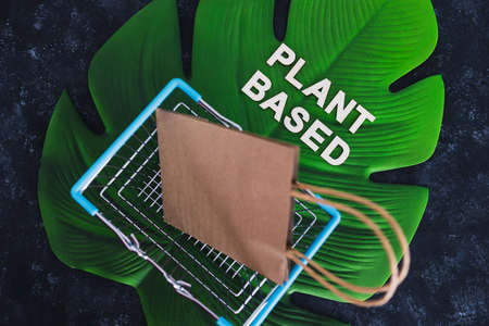 sustainable consumer choices for the environment, plant-based text with shopping cart and bag on big tropical leaf on dark backgroundの写真素材