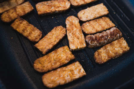 simple food ingredients concept, grilled tempeh getting cooked on griddle pan on the stoveの写真素材