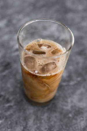 cold brew iced vanilla latte coffee in tall glass with ice on concrete background