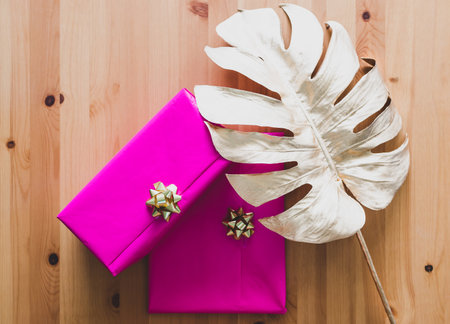 couple of birthday present wrapped up in pink and gold on wooden table with golden leaf decoration, concept of parties and celebrationsの写真素材