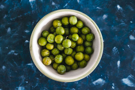 healthy plant-based food recipes concept, fresh green plums in fruit bowl on blue background