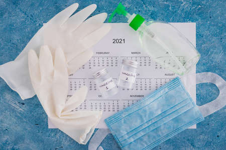vaccine and immunisation against the pandemic, ampoules with Vaccine 1 and Vaccine 2 labels side by side next to 2021 yearly calendar and gloves mask and sanitizerの写真素材