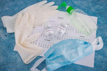 vaccine and immunisation against the pandemic, ampoules with Vaccine 1 and Vaccine 2 labels side by side next to 2021 yearly calendar and gloves mask and sanitizerの写真素材