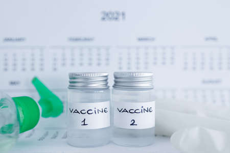 vaccine and immunisation against the pandemic, ampoules with Vaccine 1 and Vaccine 2 labels side by side next to 2021 yearly calendar and mask gloves and sanitizerの写真素材