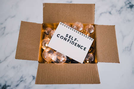 psychology and positive attitude concept, Self--confidence text on notepad surrounded by light bulbs in open box symbol of mindsetの写真素材