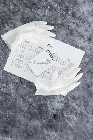vaccine against the pandemic, 2021 calendar with syringe sketch on notepad and disposable gloves on...