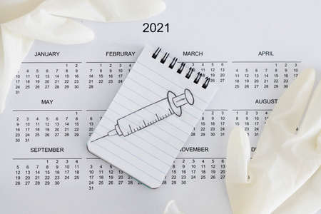 vaccine against the pandemic, 2021 calendar with syringe sketch on notepad and disposable gloves on itの写真素材