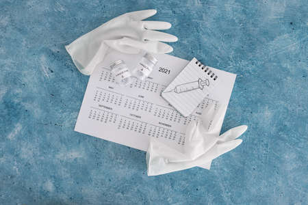 vaccine against the pandemic, 2021 calendar with syringe sketch on notepad and disposable gloves on...