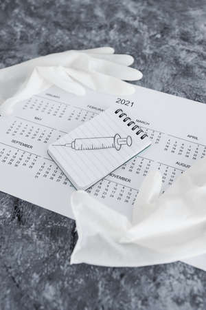 vaccine against the pandemic, 2021 calendar with syringe sketch on notepad and disposable gloves on itの写真素材