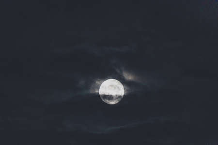 full moon with dark clouds in front of it creating a moody atmosphere in the night skyの写真素材