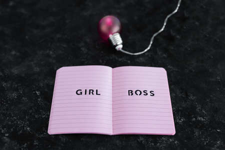 equal opportunities Girl Boss text on top of pink notebook with bright pink light bulb symbol of ideas and inventiveness on black backgroundの写真素材
