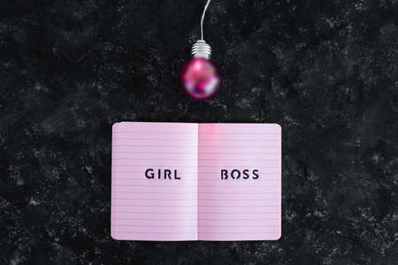 equal opportunities Girl Boss text on top of pink notebook with bright pink light bulb symbol of ideas and inventiveness on black backgroundの写真素材